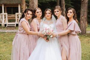 grupo retrato de el novia y damas de honor novia en un Boda vestir y damas de honor en rosado o polvo vestidos y participación elegante ramos de flores en el Boda día. foto