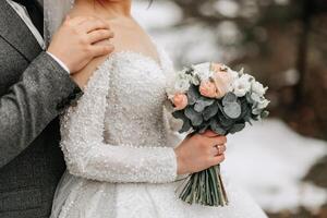 Portrait. The bride and groom are standing, holding a bouquet, posing. Emphasis on the bouquet. A walk in the forest. Winter wedding photo