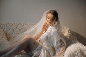 Nice cute girl in a boudoir robe. Happy beautiful bride under veil. Fashion, beauty, style. Morning of the bride. Beautiful bride with stylish make up and hair style. photo