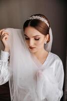 A beautiful brunette bride with a tiara in her hair is getting ready for the wedding in a beautiful robe in boudoir style. Close-up wedding portrait, photo. photo