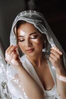 A beautiful brunette bride with a tiara in her hair is getting ready for the wedding in a beautiful robe in boudoir style. Close-up wedding portrait, photo. photo