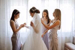 Morning of the bride. The bride's maid of honor helps the bride lace up her dress, fasten buttons on the dress or sleeves. Girlfriends help the bride fasten her dress photo