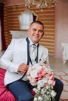 Stylish portrait of the groom with a bouquet of flowers. A man is preparing for a wedding ceremony in the morning. Groom's morning. Preparation for the groom's morning. Young and handsome groom. photo