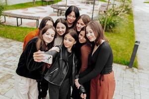 Friends taking a big group selfie smiling at the camera - laughing young people standing outdoors and having fun - portrait of cheerful schoolchildren outside school - human resources concept photo