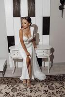 Full length portrait of a bride in a luxurious elegant wedding dress with a long veil standing near a mirror in a bright studio. photo