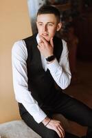 Cropped photo of groom in white shirt buttoning black vest. Business style. A stylish watch