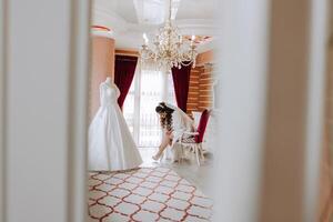 A happy bride is preparing for her luxurious wedding in a hotel room, with a wedding dress on a mannequin nearby. Portrait of a woman with fashionable hair, makeup and a smile in a dressing gown. photo