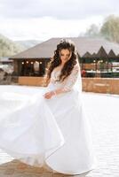 Curly bride twirls in her wedding dress. Magnificent dress with long sleeves, open bust. Summer wedding photo