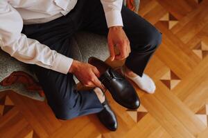 un elegante hombre usa negro cuero formal zapatos. atadura zapatos. negocio hombre atadura cordones de los zapatos en el piso. arriba cerca el novio es preparando para el boda. foto