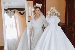 portrait of a luxurious bride in boudoir style near a mirror with reflection. Preparing the bride for the wedding in the morning in a white robe. photo