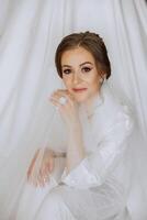 A beautiful brunette bride with a tiara in her hair is getting ready for the wedding in a beautiful robe in boudoir style. Close-up wedding portrait, photo. photo