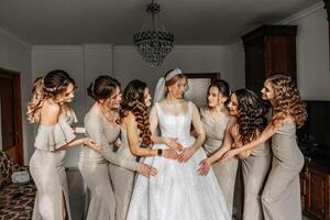 el novia en un blanco vestido, velo y novias en crema vestidos, posando en hermosa Encendiendo. Mañana de el novia foto