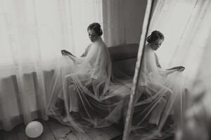 portrait of a luxurious bride in boudoir style near a mirror with reflection. Preparing the bride for the wedding in the morning in a white robe. photo