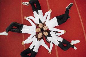 Happy friends lying together in a circle looking at the camera, holding hands and smiling while lying on a red wall... Friendship, lifestyle, togetherness, business and teamwork concepts. photo