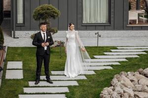 Portrait. The bride in an elegant long dress and the groom are hugging and posing in the yard, standing on a stone path. Wedding in nature photo