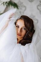 A beautiful brunette bride with a tiara in her hair is getting ready for the wedding in a beautiful robe in boudoir style. Close-up wedding portrait, photo. photo