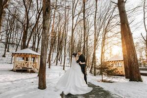 Winter wedding. A happy couple in wedding clothes are hugging and smiling in a winter park covered with snow on their wedding day. Winter love story of a beautiful couple in snowy winter weather photo
