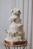 A large luxurious multi-tiered wedding cake is decorated with fresh white rose flowers in the banquet hall. Wedding dessert under the evening light. Wedding decor. photo