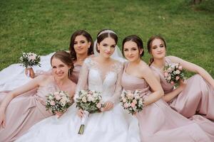 Group portrait of the bride and bridesmaids. Bride in a wedding dress and bridesmaids in pink or powder dresses and holding stylish bouquets on the wedding day. photo