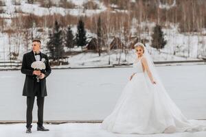 The bride and groom are walking in the winter garden. Winter photo session in nature. The groom is holding a bouquet.