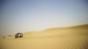 Aerial view on Off-road adventure with SUV in Arabian Desert at sunset with Dubai skyline or cityscape. Desert touring with SUV. Offroad SUV riding in the desert. Driving a 4-wheel drive SUV on the video