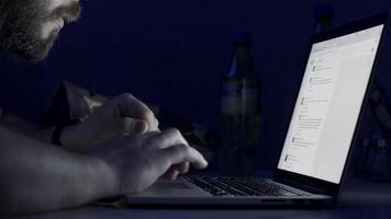 Man with a beard working late at night on the computer. Young man reading news on laptop lying in dark room. Looking concentrated. man with laptop sitting in a dark room video