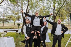 Cheerful, young, energetic witnesses of the groom next to the groom. Friends congratulate the groom. Groom and his funny friends having fun on the wedding day of the newlyweds. photo