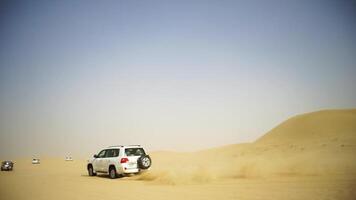 Antenne Aussicht auf Offroad Abenteuer mit suv im arabisch Wüste beim Sonnenuntergang mit Dubai Horizont oder Stadtbild. Wüste Touring mit SUV. Offroad suv Reiten im das Wüste. Fahren ein 4-Rad Fahrt suv auf das video