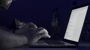 Man with a beard working late at night on the computer. Young man reading news on laptop lying in dark room. Looking concentrated. man with laptop sitting in a dark room video