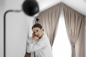 un hermosa y confidente novia en blanco pijama con un largo velo poses para un fotógrafo en un hotel habitación. Boda concepto. Mañana de el novia. preparación para el boda. foto