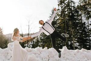 el novia y novio son corriendo a lo largo un Nevado la carretera en contra el antecedentes de un pino bosque y hermosa contraste luz de sol. lado vista. invierno boda. sitio para logo. foto