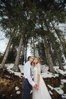 A young couple, the bride and groom, smilingly show off their wedding rings against the background of tall trees. Have a good time laughing. Winter wedding photo