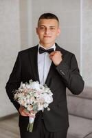 A stylish groom is tying his tie, preparing for the wedding ceremony. Groom's morning. A businessman wears a tie. The groom is getting ready in the morning before the wedding ceremony. photo