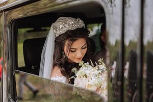 A beautiful bride, sitting in a car, looks out of the open window of the car. A beautiful bride with a bouquet of flowers in her hands is sitting in a stylish expensive car. photo