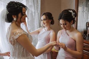 Morning of the bride. The bride's maid of honor helps the bride lace up her dress, fasten buttons on the dress or sleeves. Girlfriends help the bride fasten her dress photo