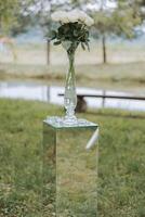A vase with white roses on a mirror stand. Wedding in nature. Details photo