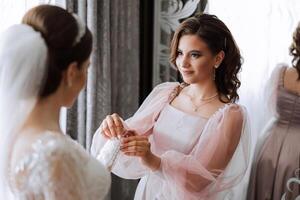 Morning of the bride. The bride's maid of honor helps the bride lace up her dress, fasten buttons on the dress or sleeves. Girlfriends help the bride fasten her dress photo