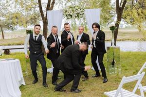 Cheerful, young, energetic witnesses of the groom next to the groom. Friends congratulate the groom. Groom and his funny friends having fun on the wedding day of the newlyweds. photo