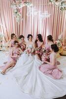 Group portrait of the bride and bridesmaids. Bride in a wedding dress and bridesmaids in pink or powder dresses and holding stylish bouquets on the wedding day. photo