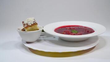 Borsch in plate with wood spoon and black bread isolated on white. Vegetables and meat in red beetroot soup or borsch with sour cream. bread, green onion, parsley. video