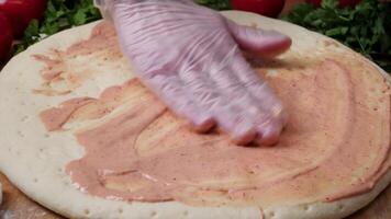 de cerca mano de cocinero panadero en blanco uniforme haciendo Pizza a cocina. marco. Cocinando Pizza. el pieza de trabajo vertido tomate salsa. cocinero asperja queso pizza, un lote de queso en un pizza, Cocinando proceso video