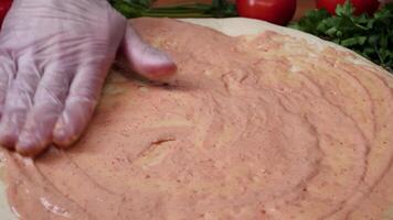 Adding sauce. Italian pizza preparation. Frame. Cheese being spread on tomato sauce on pizza base. Closeup hand of chef baker in white uniform making pizza at kitchen video