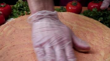 Adding sauce. Italian pizza preparation. Frame. Cheese being spread on tomato sauce on pizza base. Closeup hand of chef baker in white uniform making pizza at kitchen video