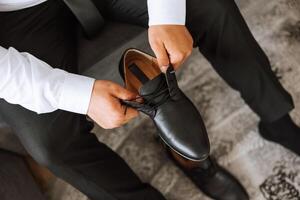 un elegante hombre usa negro cuero formal zapatos. atadura zapatos. negocio hombre atadura cordones de los zapatos en el piso. arriba cerca el novio es preparando para el boda. foto