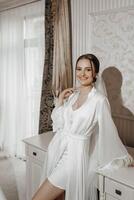 portrait of bride girl in white robe with professional hairstyle and natural makeup in hotel room with gorgeous interior photo