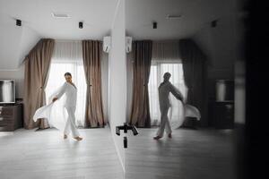 young beautiful bride in white pajamas in the morning. The bride's morning at the hotel. Long fashionable veil. Mirror photo