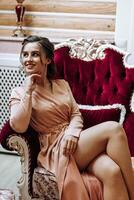 retrato de un joven hermosa elegante mujer sentado y posando en un rojo ante Sillón en Arte Nouveau estilo. hermosa modelo niña en un lujoso noche vestido. dama con Perfecto constituir. foto