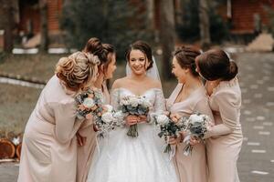 un morena novia en un blanco elegante vestir y su amigos en gris vestidos actitud con ramos de flores Boda retrato en naturaleza, Boda foto en ligero colores.