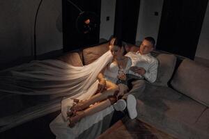 portrait of the newlyweds in the hotel lying on the couch with glasses of champagne. The groom gently touches the bride. After the wedding ceremony. Happy bride and groom celebrating photo