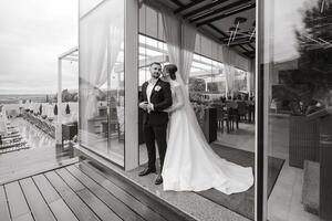 linda recién casados son suavemente abrazando y sonriente cerca el restaurante. retrato de el novia y novio en un cordón vestido. foto